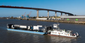 Barge et bateaux pousseurs transportant des camions devant le pont de Saint-Nazaire