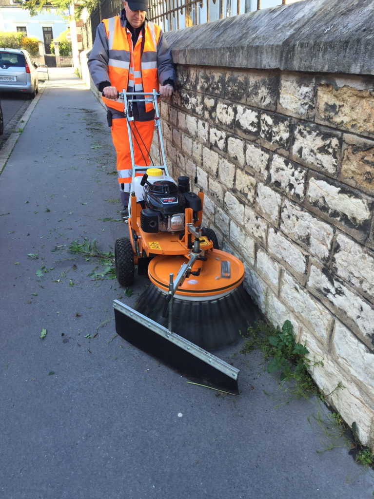 Comme l'éco-pâturage, le désherbage mécanique fait partie des techniques alternatives d'entretien des espaces verts. Ici, une désherbeuse mécanique à brosse poussée par un agent "espaces verts".
