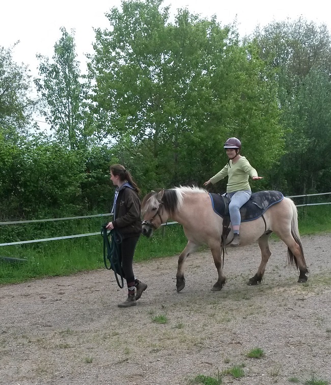 Jeune handicapée en situation de handicap mental faisant du cheval sans les mains, la longe du cheval est tenue par une encadrante