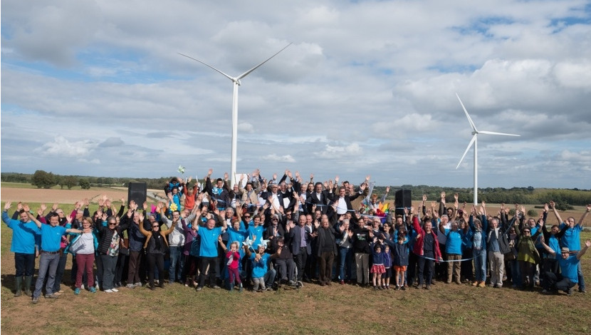 groupe d'habitants investis dans une des coopératives citoyennes d'énergie, posant devant leur éolienne en arrière plan