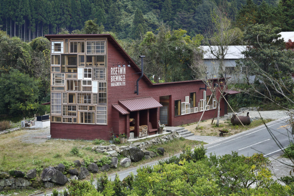 Exemple surprenant d'économie circulaire : bâtiment en bois avec une grande façade entièrement vitrée composée de nombreuses fenêtres de récupération de toutes formes.