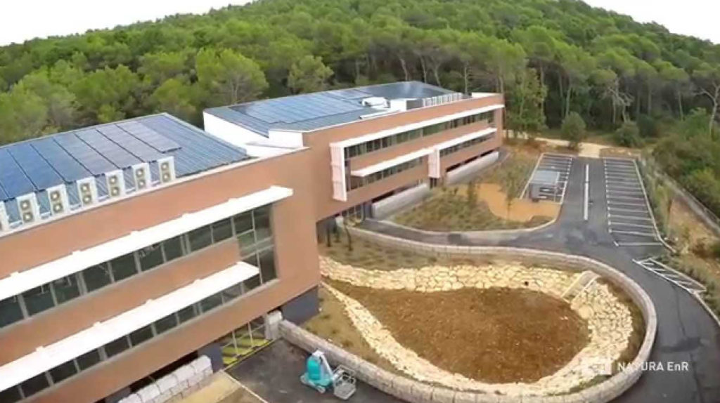 Vue extérieur des bâtiments : larges façades sud vitrées, brises soleil, panneaux photovoltaïques sur les toits. Bâtiments positifs illustrant l'économie circulaire